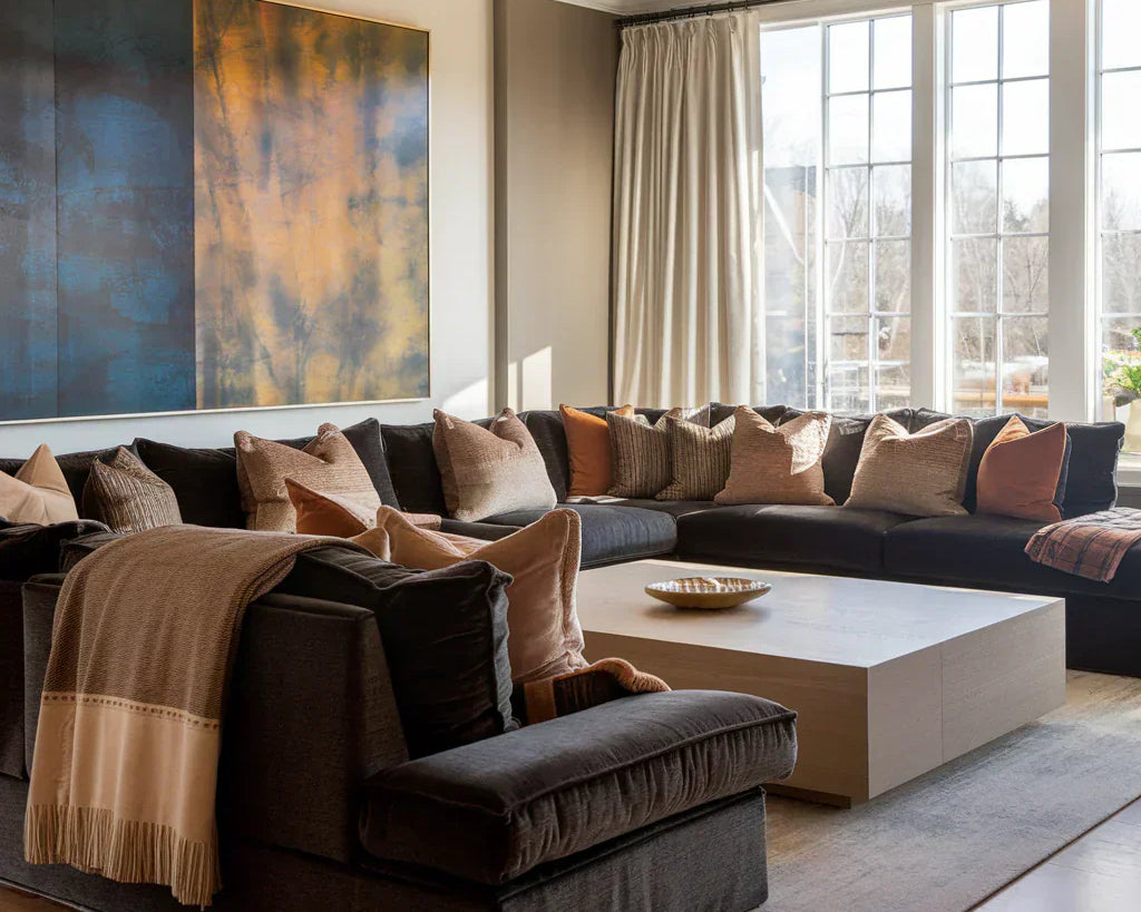 A photo of a living room with a luxurious ambiance. There's a large sectional sofa in a dark gray hue, with plush pillows in various textures and patterns.