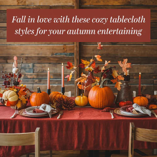 A photo of a cozy table setting with a red tablecloth and autumn-themed decorations. There are pumpkins, leaves, and candles on the table. The background is a rustic wooden wall