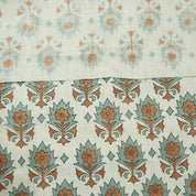 May include: Close-up view of two fabric swatches showcasing a subtle, repeating floral pattern. The top swatch displays a lighter, more faded pattern in muted teal and beige, while the bottom swatch features a bolder, more defined pattern in teal and burnt orange. Both fabrics share a similar base color of off-white or beige linen, creating a cohesive design. The patterns are reminiscent of traditional block-printed textiles, suggesting a handcrafted or vintage aesthetic.