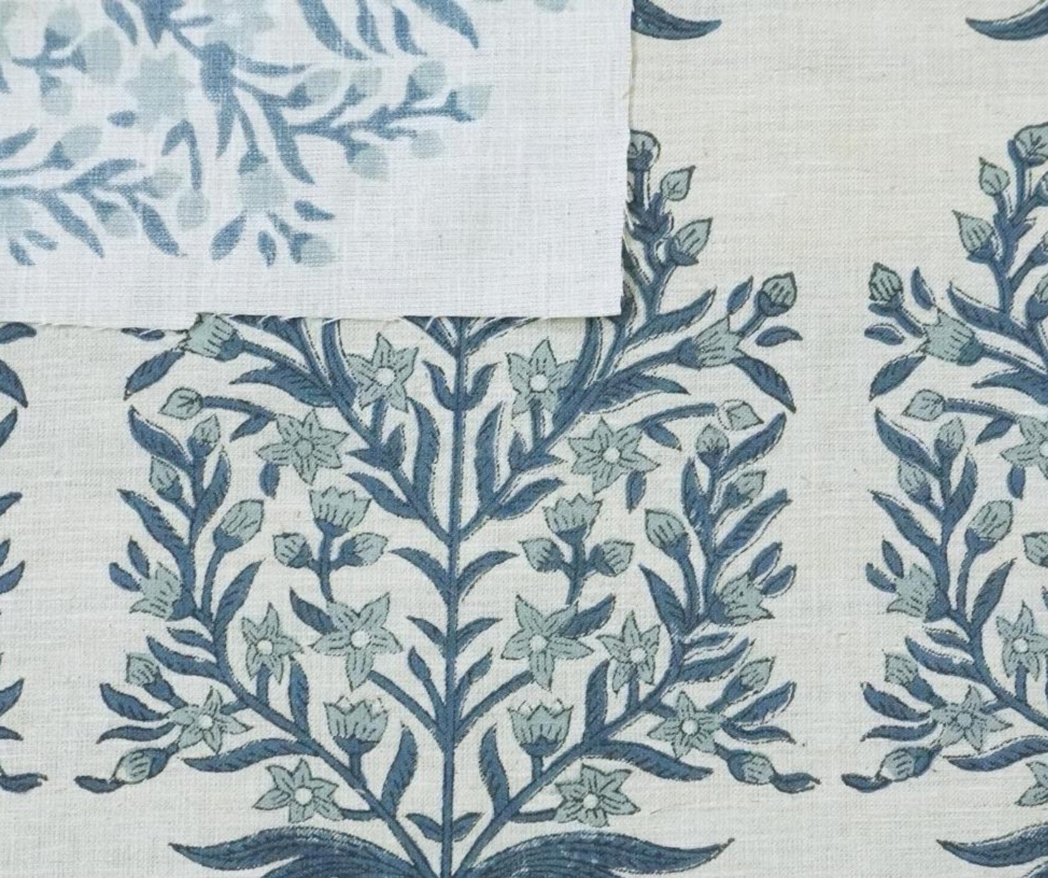 May include: Close-up view of Vrindavan linen blend fabric in natural color, 58' wide. The textile features a repeating pattern of stylized floral motifs in shades of blue-green on a light beige background. The design is reminiscent of traditional Indian block printing.  The print name and fabric details are visible at the bottom.