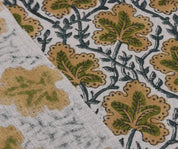 Close-up of fabric with a floral pattern featuring green and beige leaves on a white background.